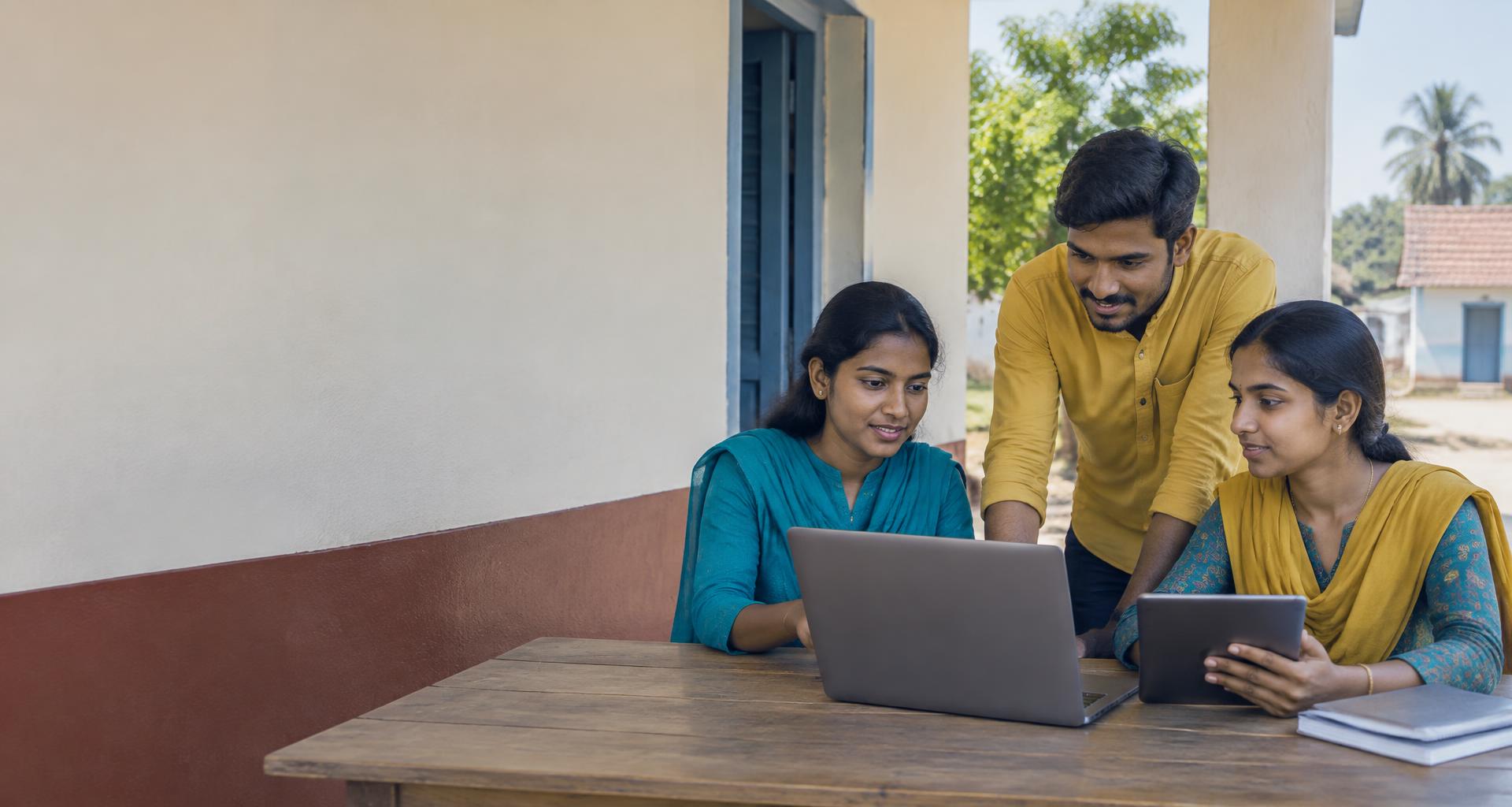 Three village volunteers collaborating with a laptop and tablet